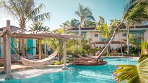 A pool area with a hammock, lounge chairs, and palm trees. - Boardwalk Boutique Hotel Aruba - Adults Only (Noord)