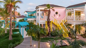 A multi-story hotel with a pink and blue exterior, a central staircase, and a well-maintained garden with palm trees. - Boardwalk Boutique Hotel Aruba - Adults Only (Noord)