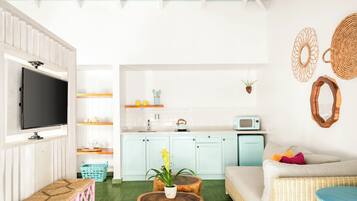 Una sala de estar moderna con un televisor de pantalla plana, un sofá, una mesa de centro y una zona de cocina con microondas y armarios.