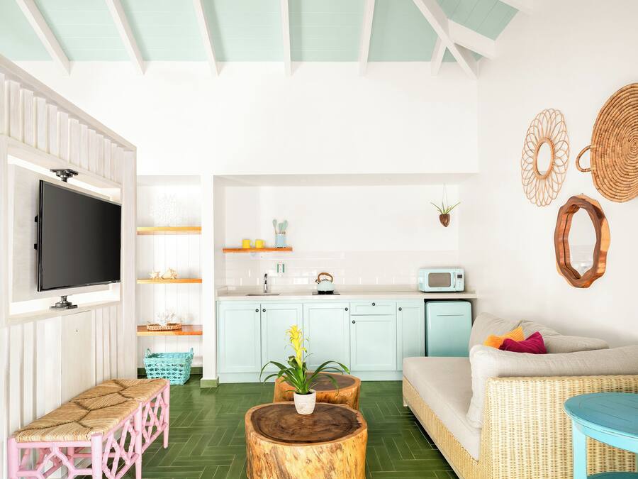 Una sala de estar moderna con un televisor de pantalla plana, un sofá, una mesa de centro y una zona de cocina con microondas y armarios.