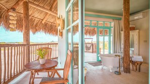 A wooden deck with a table and chairs, a thatched roof, and a view of the ocean. - Boardwalk Boutique Hotel Aruba - Adults Only (Noord)