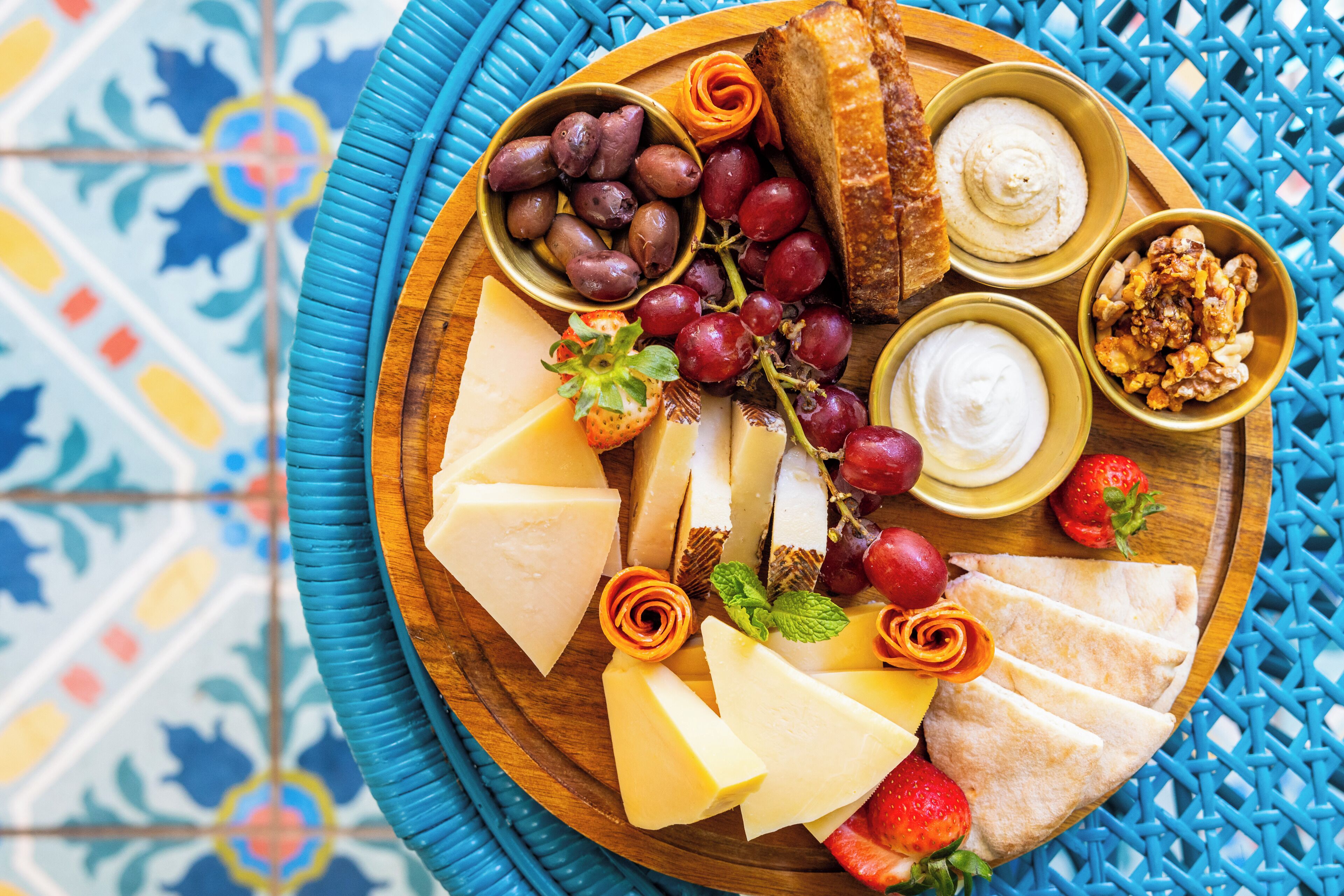 A wooden board with various cheeses, grapes, strawberries, and nuts.