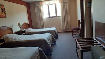 A hotel room with two beds, a desk with a lamp, a chair, and a radiator.