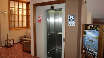 An elevator with a safety sign, a chair, a window, and a poster on the wall.