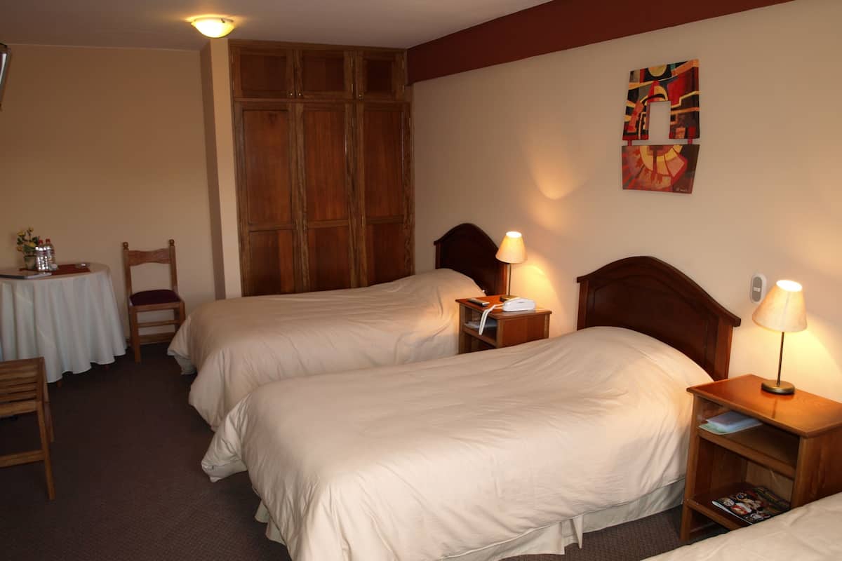 Ett hotellrum med två sängar, en garderob i trä, ett bord med en stol och en tavla på väggen.