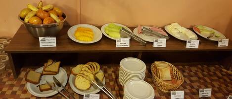 A buffet with various food items including fruits, cheese, ham, and bread.