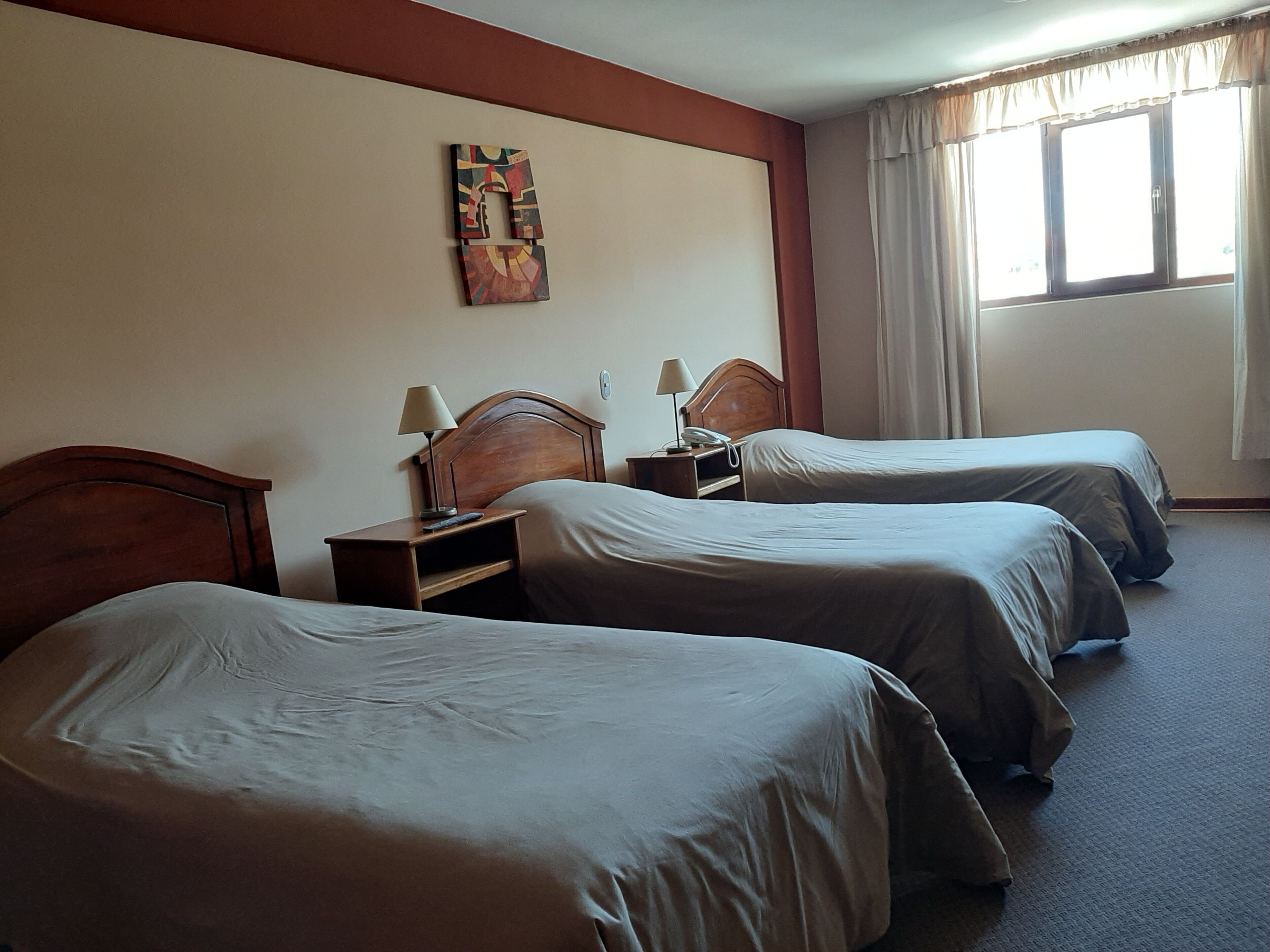 A hotel room with two single beds, a wooden headboard, a bedside table with a lamp, and a painting on the wall.