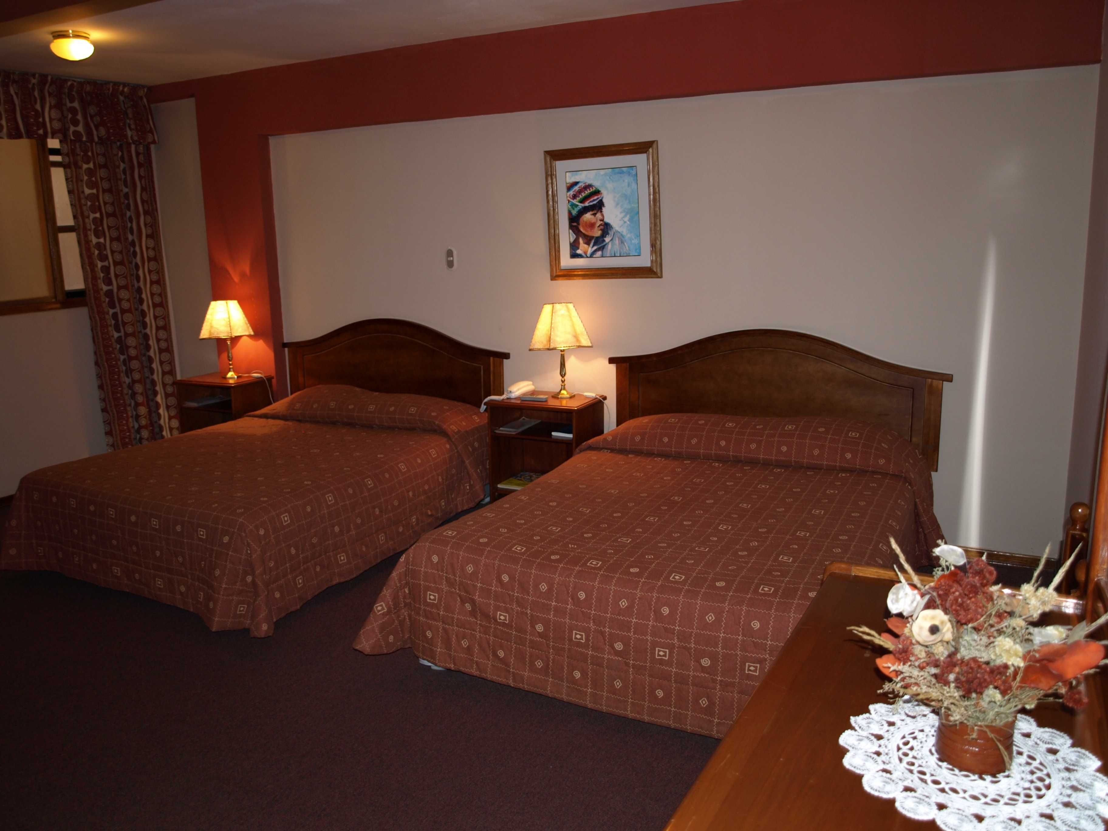 A hotel room with two beds, a nightstand with lamps, a framed picture on the wall, and a table with a vase of flowers.