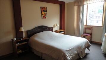 Une chambre d’hôtel avec un grand lit, une table de chevet avec une lampe, une chaise et une fenêtre avec des rideaux.