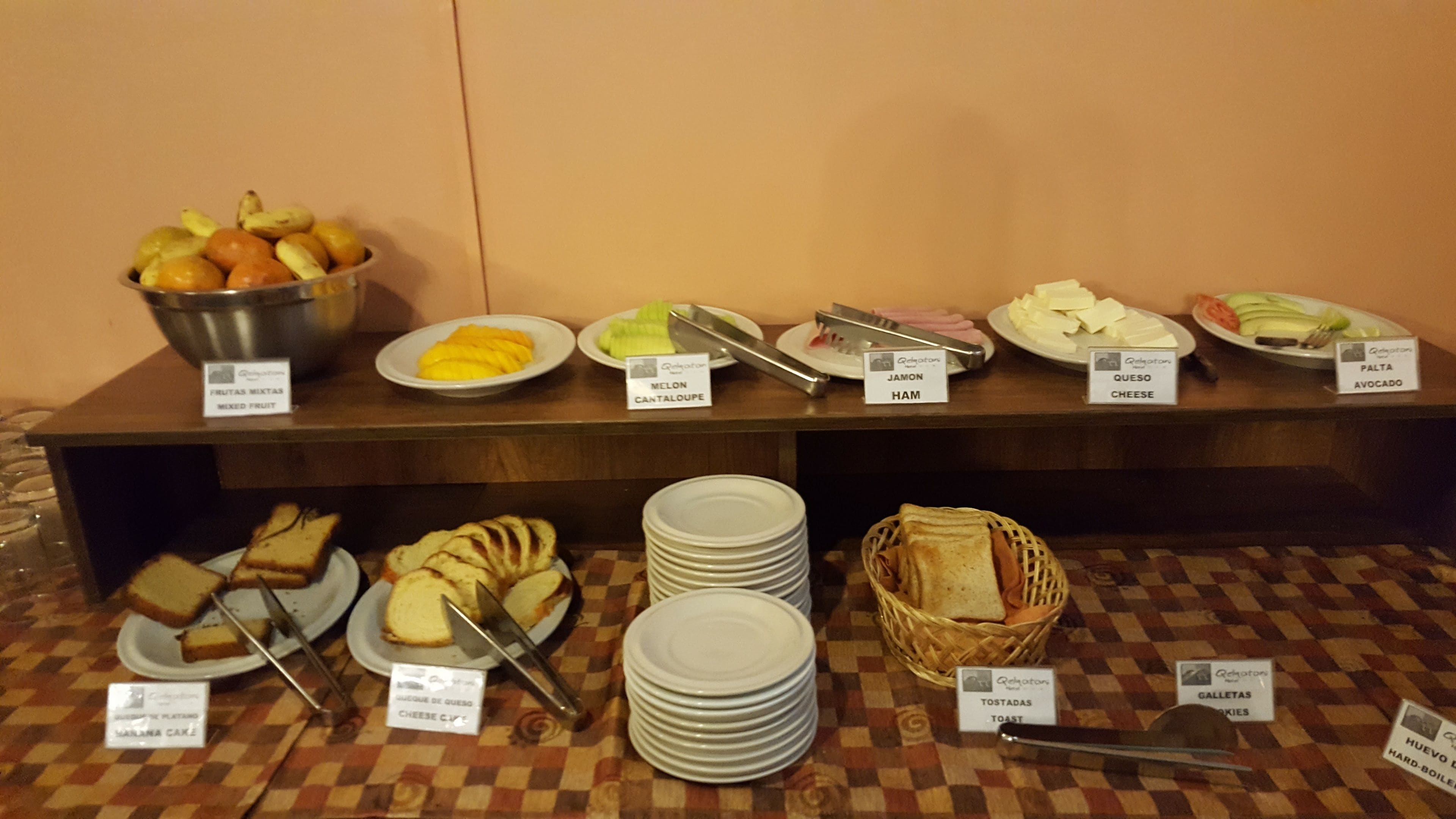 Un bufé con una variedad de alimentos, incluyendo fruta mixta, melón cantalupo, melón, jamón, queso, aguacate, tostadas y huevos cocidos.