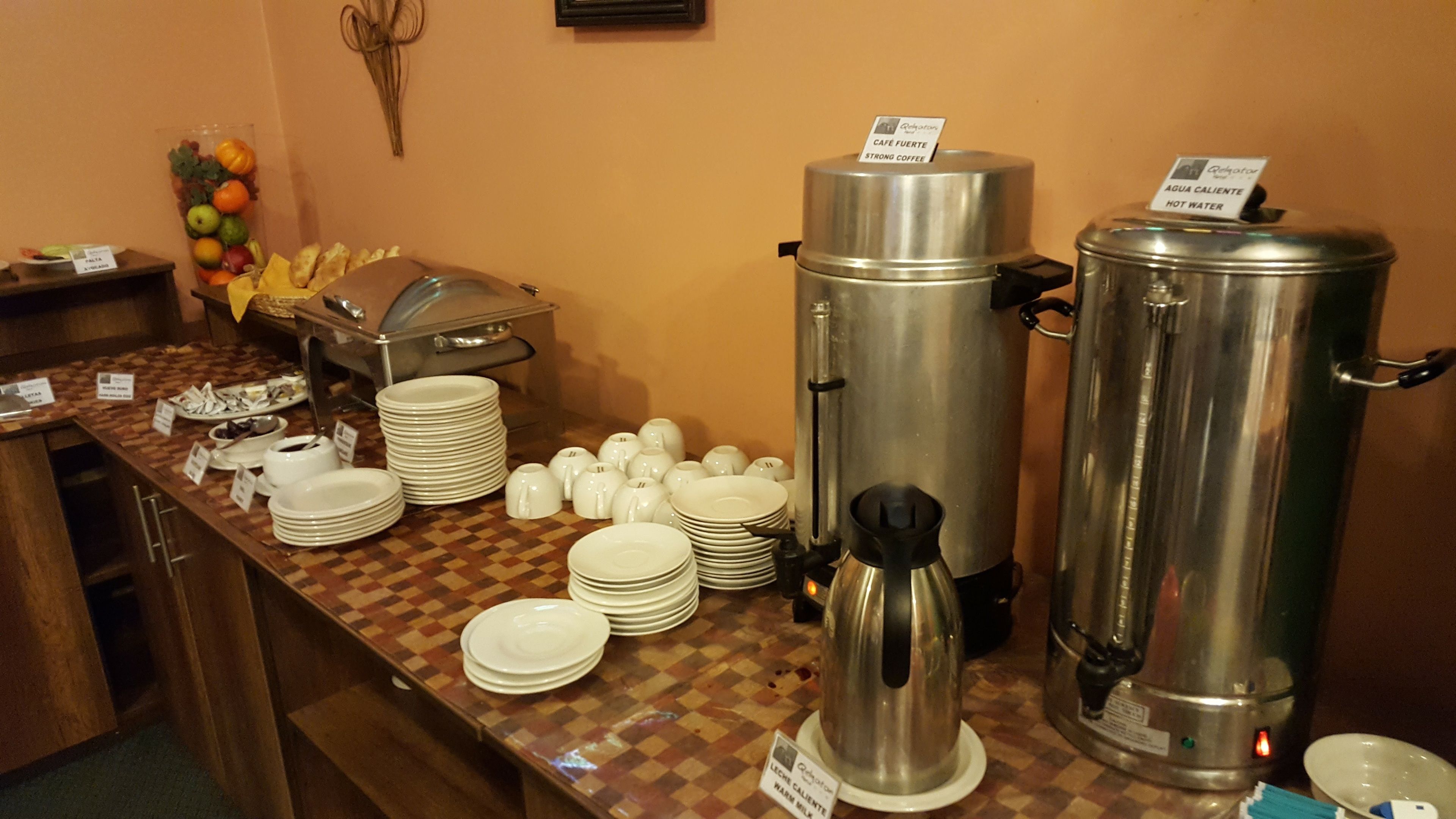 Montaje de bufé con varias estaciones de comida, que incluyen un dispensador de agua caliente y una estación de café.