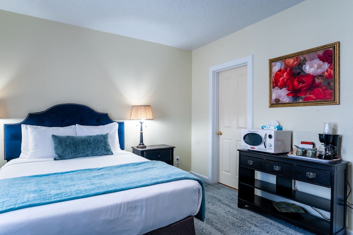 A hotel room with a bed, a bedside lamp, a microwave, a coffee maker, and a painting on the wall.