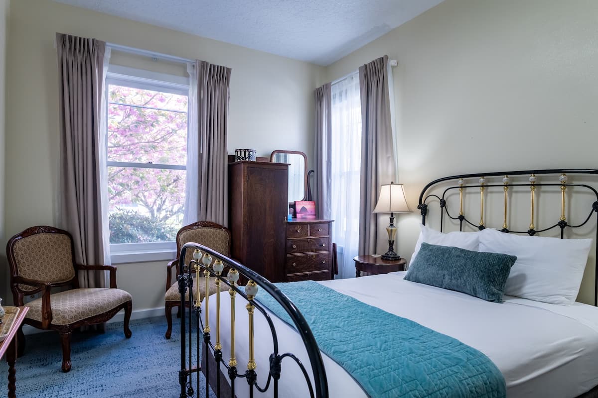 A bedroom with a bed, two chairs, a dresser, and a window with curtains.