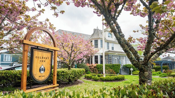 Letrero del Gilbert Inn con un diseño clásico, rodeado de árboles en flor y jardines bien cuidados.