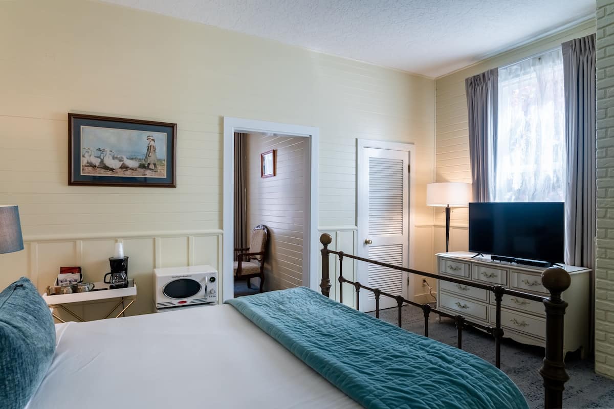 A hotel room with a bed, a television, a dresser, a microwave, a chair, and a painting on the wall.