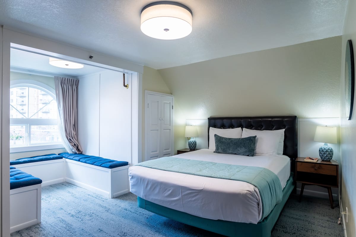 A bedroom with a bed, bedside lamps, a window with curtains, and a built-in bench.