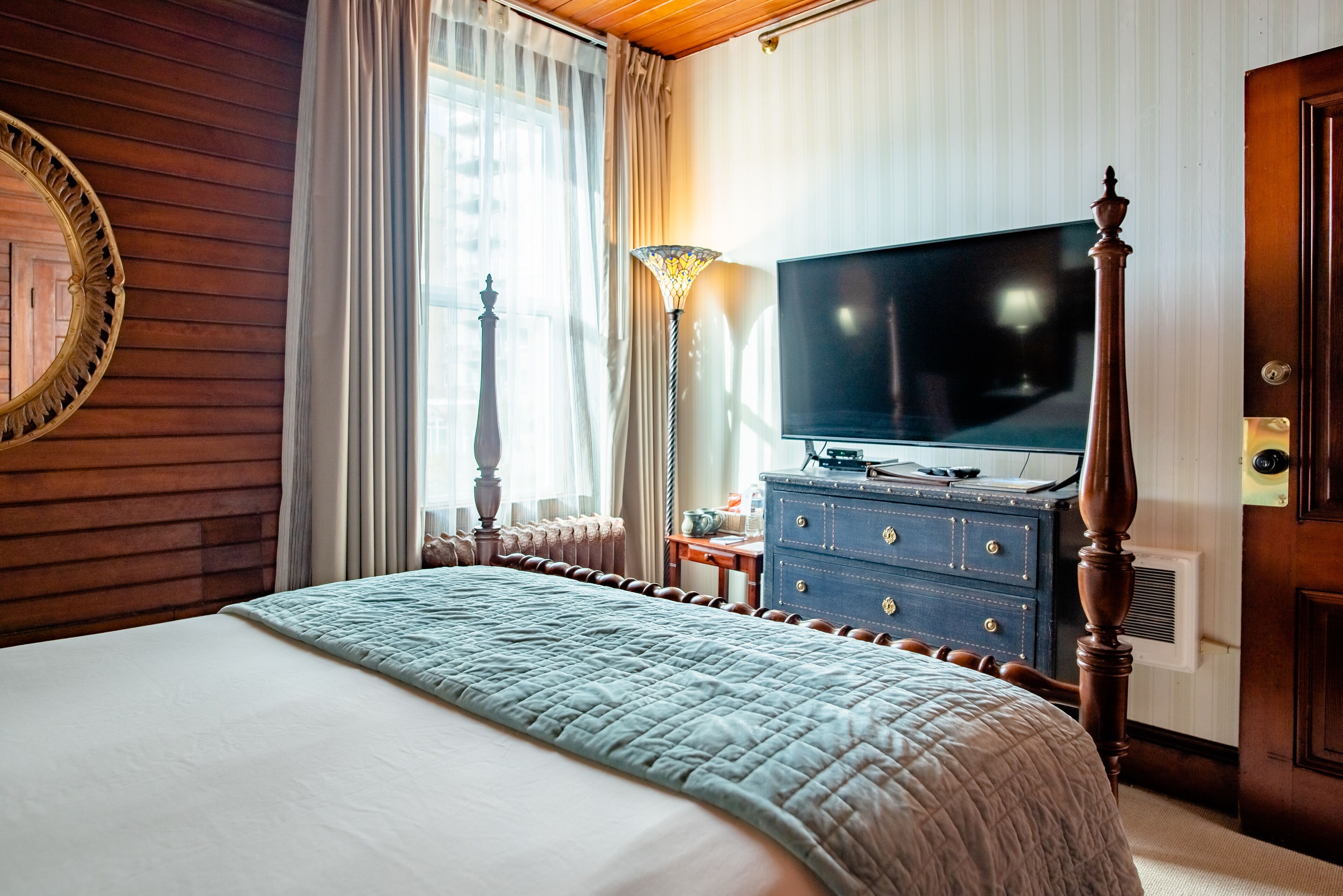 Una camera d'albergo con un letto grande, una televisione, un comò e una lampada.