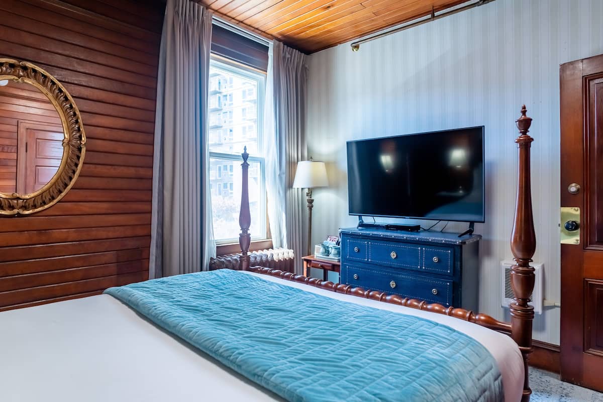 A hotel room with a large bed, a television, a dresser, and a window with curtains.