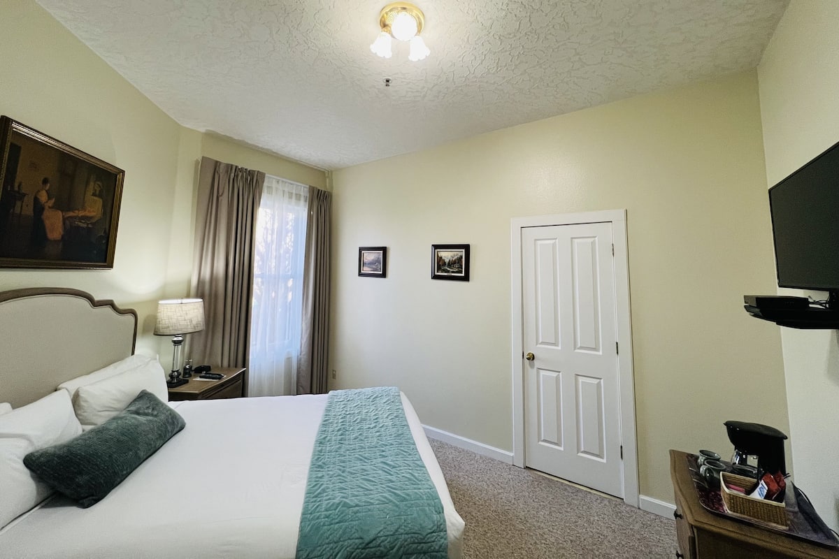 A hotel room with a bed, a nightstand, a lamp, a television, and a door.