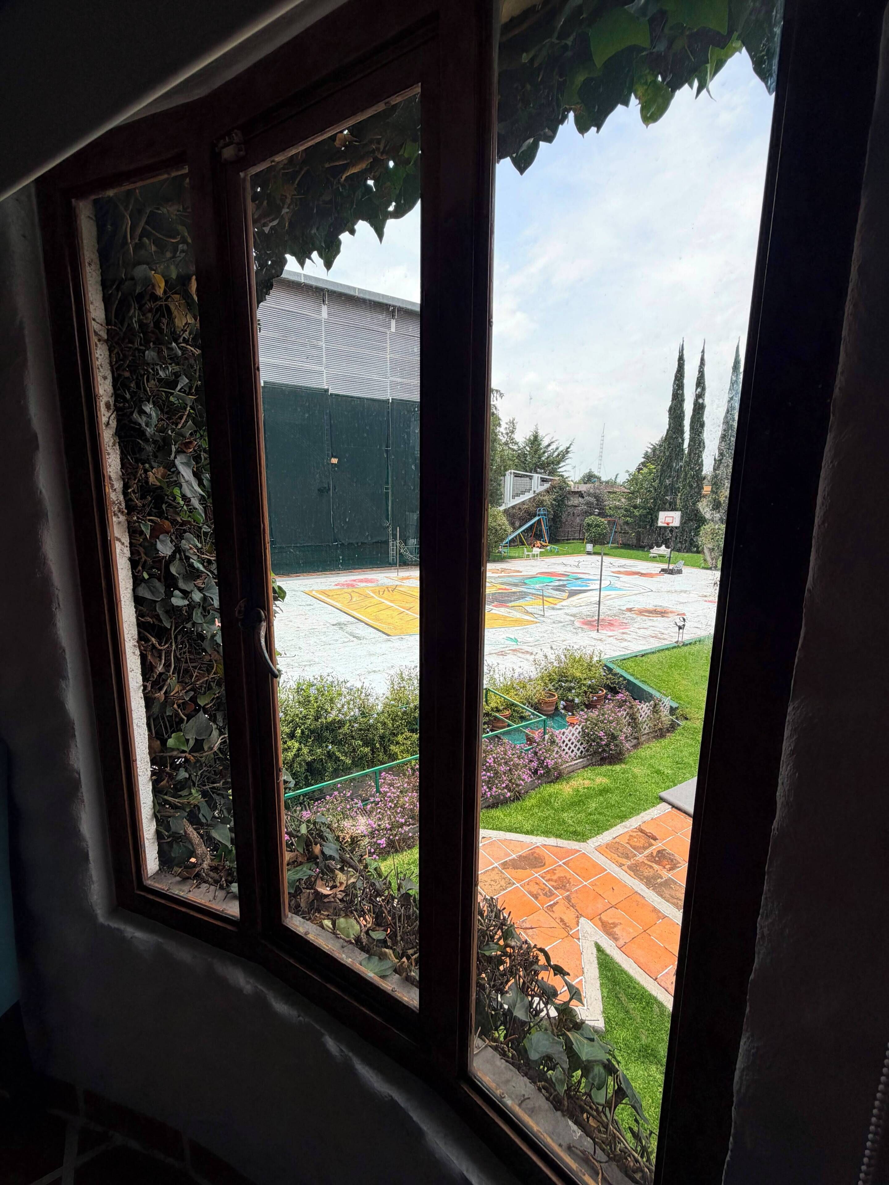 A window with a view of a basketball court, a green building, and a garden area.
