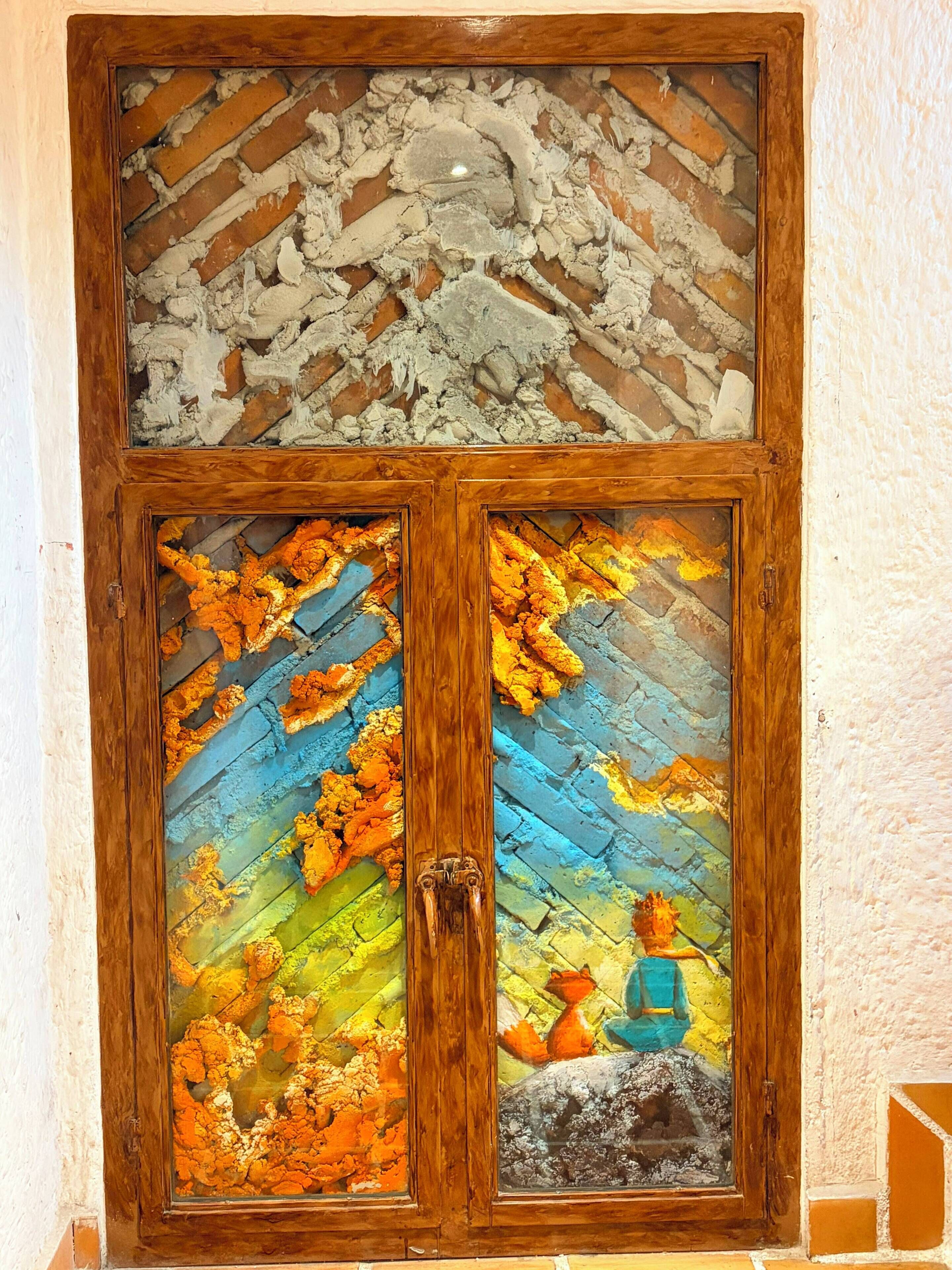 Una ventana de madera con un muro de ladrillo y un mural colorido.