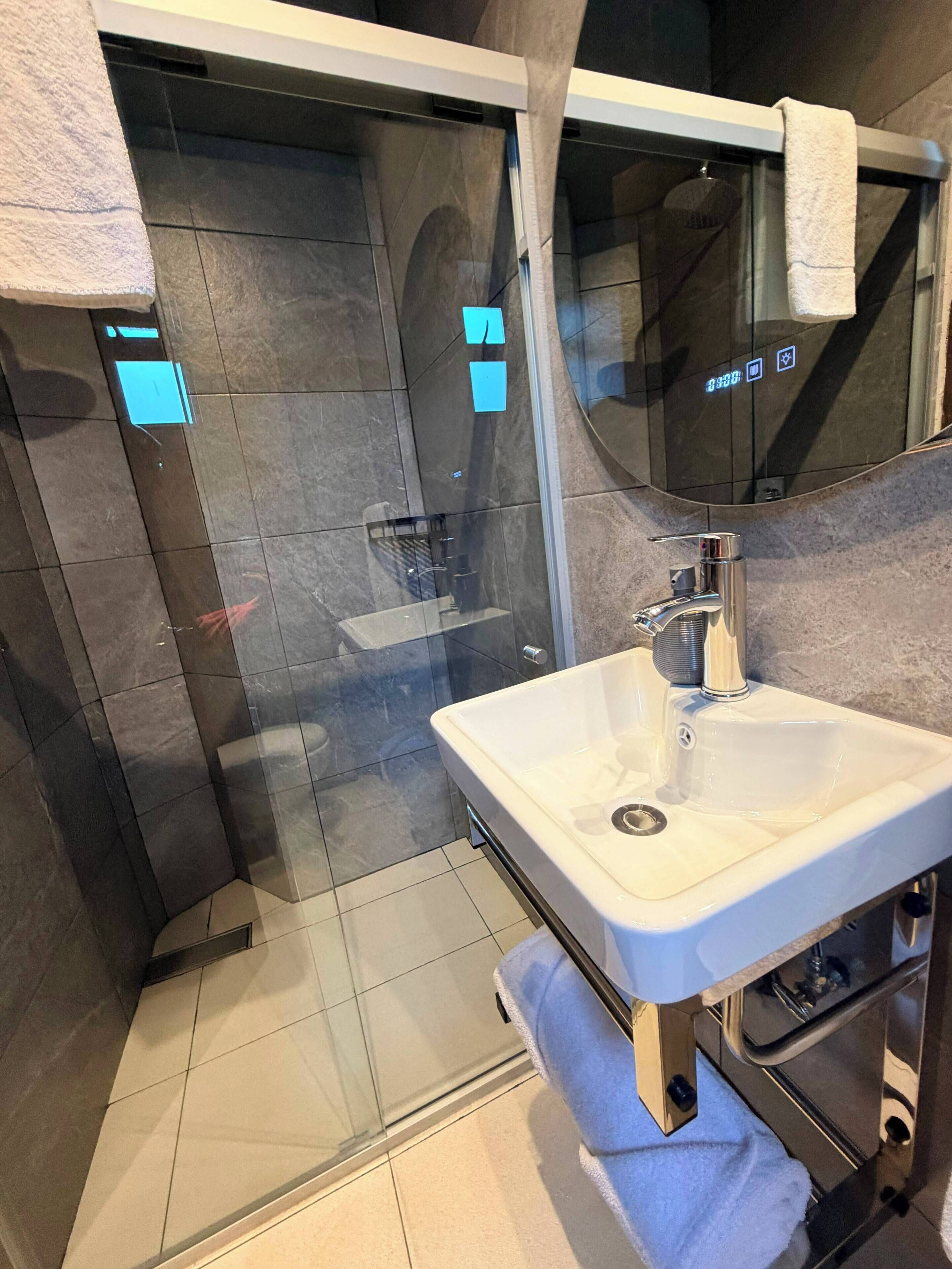 A modern bathroom with a glass-enclosed shower, a white sink, and a towel rack.