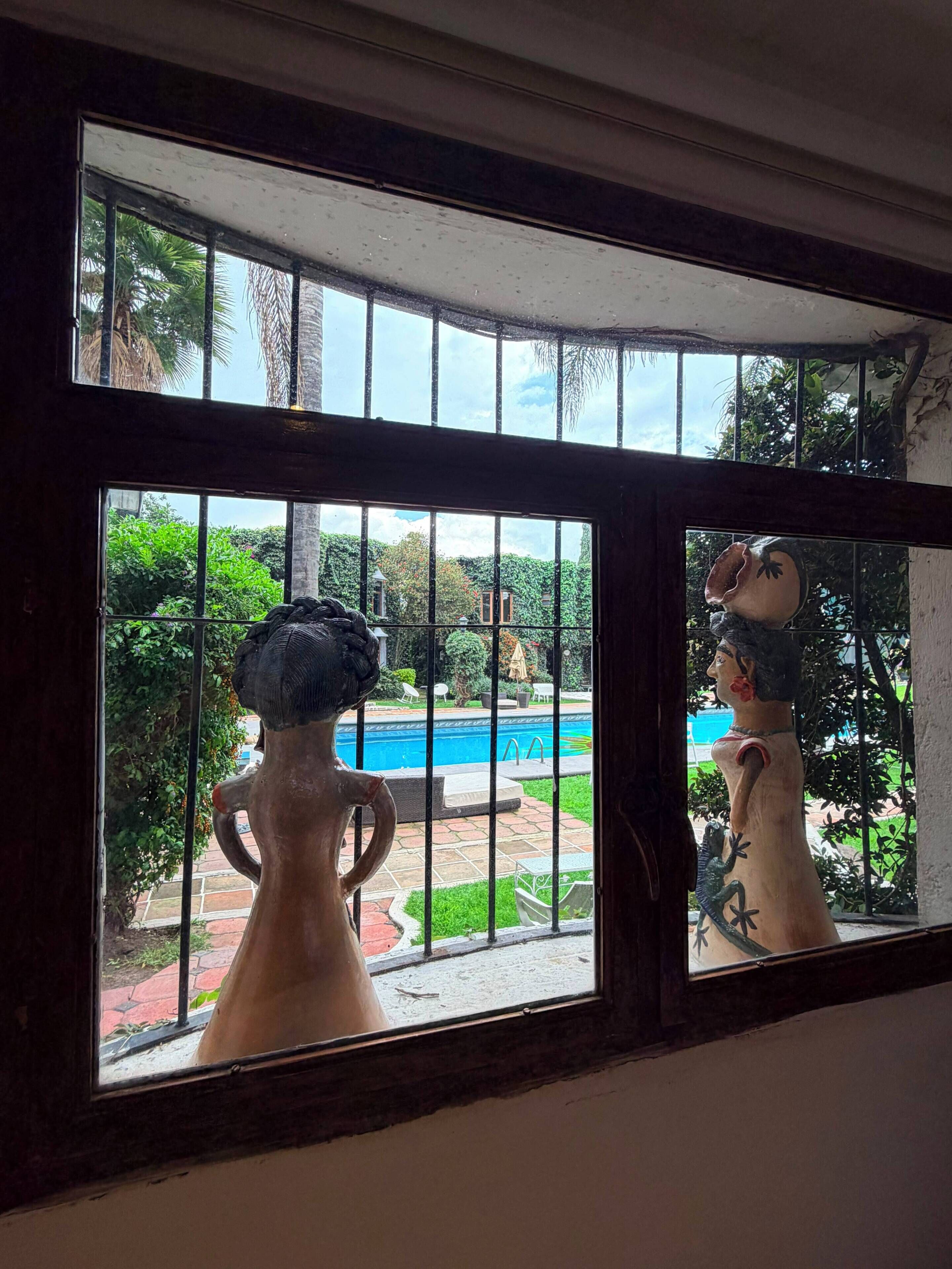 A view through a window with a decorative vase and a statue of a woman.