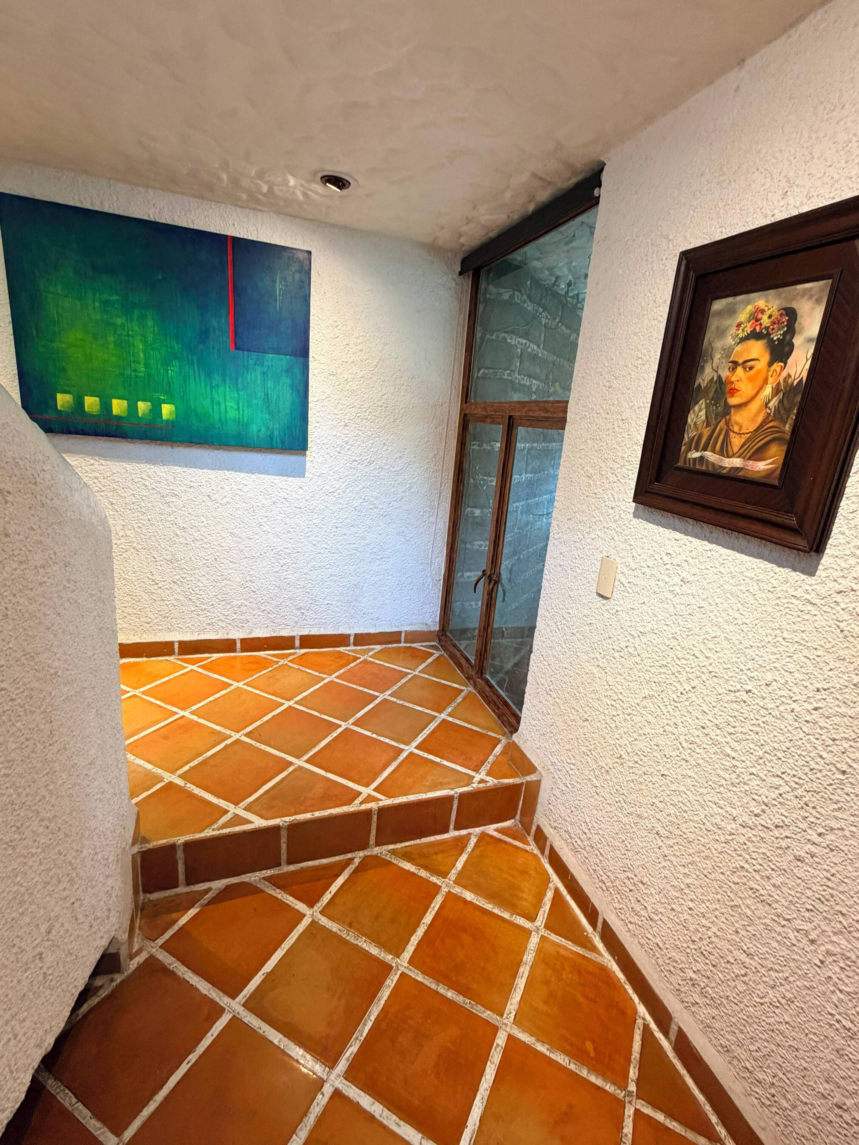 A corner with a tiled floor, a painting on the wall, and a framed picture.