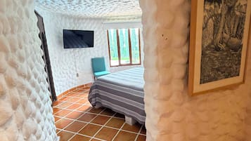 A room with a unique textured ceiling, a bed with striped bedding, a television on the wall, and a framed artwork.