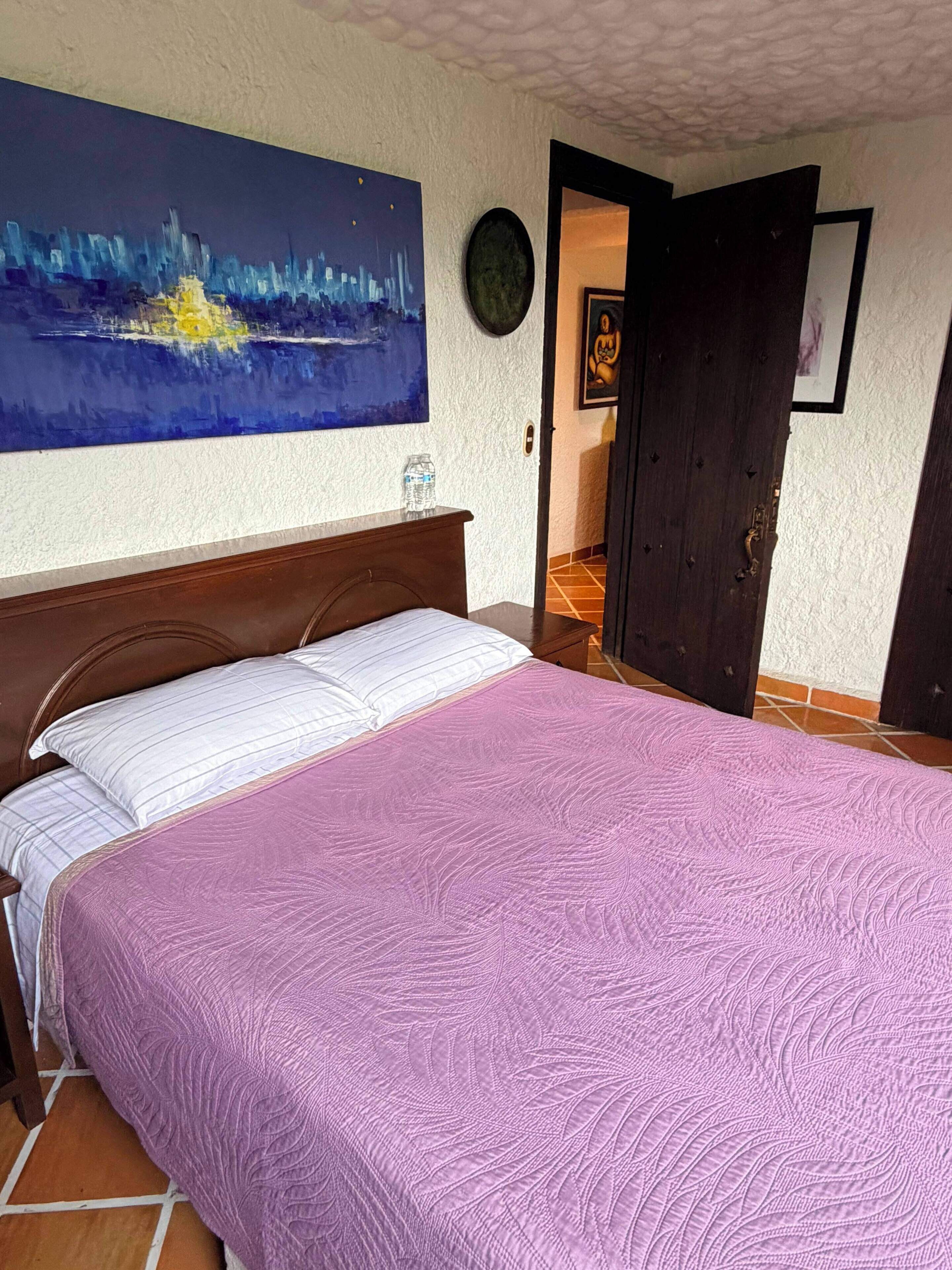 Un dormitorio con cama, un cuadro en la pared y una puerta que da a otra habitación.