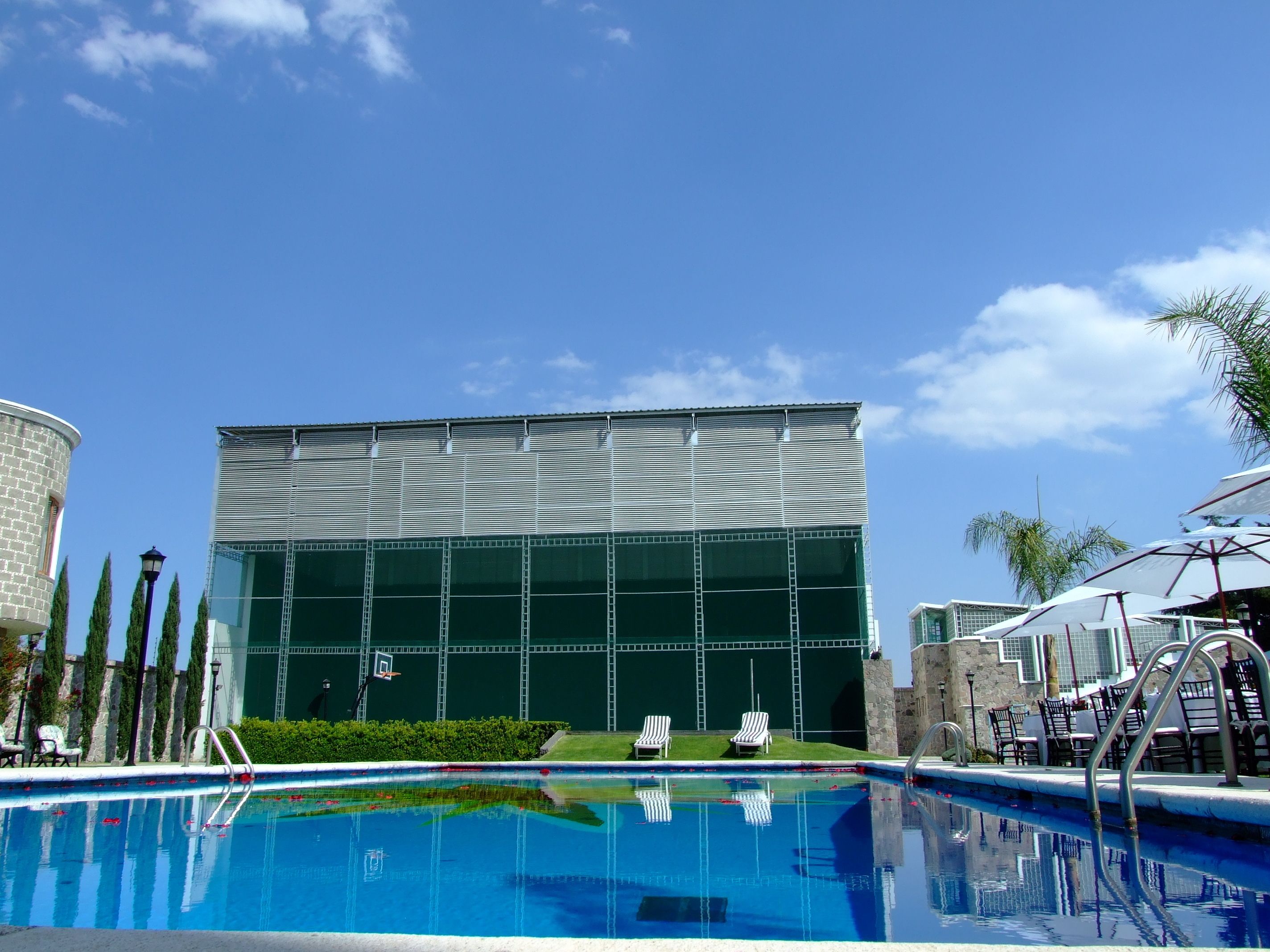 A swimming pool with a modern building in the background, a stone tower, and a palm tree.