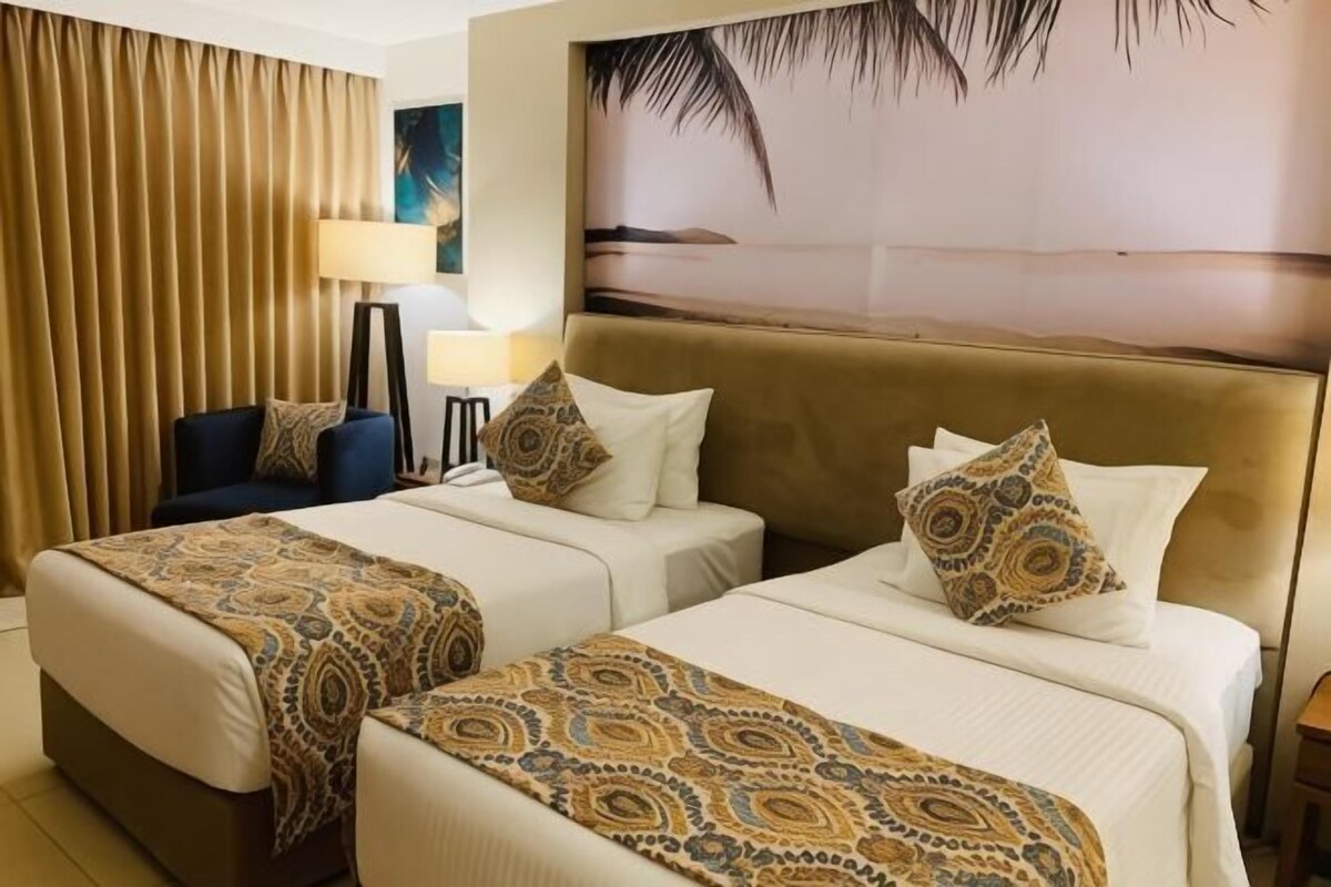 Une chambre d’hôtel avec deux lits, un canapé, une lampe et un tableau représentant une scène de plage.