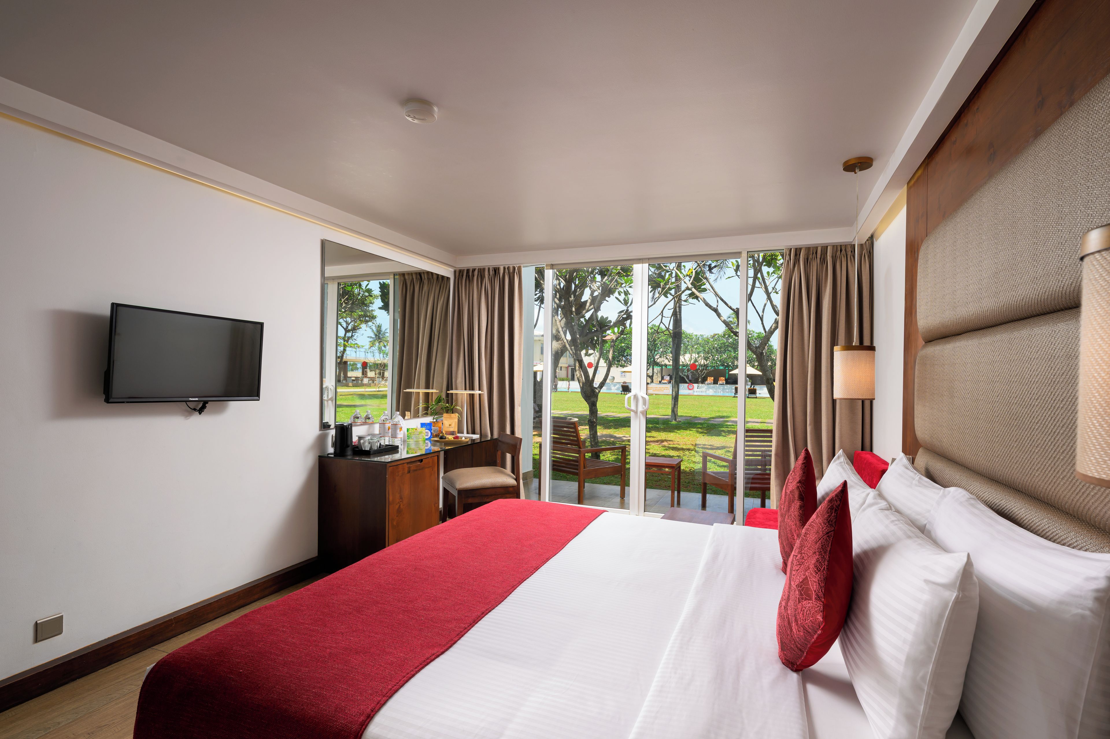 A hotel room with a large bed, a desk, a television, and a view of the outdoors.
