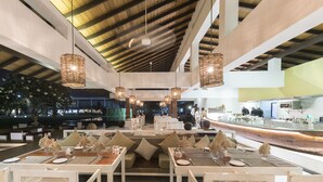 Un restaurante moderno con techos altos, candelabros de mimbre colgantes y una barra larga.