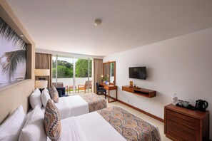 A hotel room with two beds, a desk, a chair, a TV, and a balcony with a view of greenery. - Pegasus Reef - A Beach Resort in Colombo (Wattala)