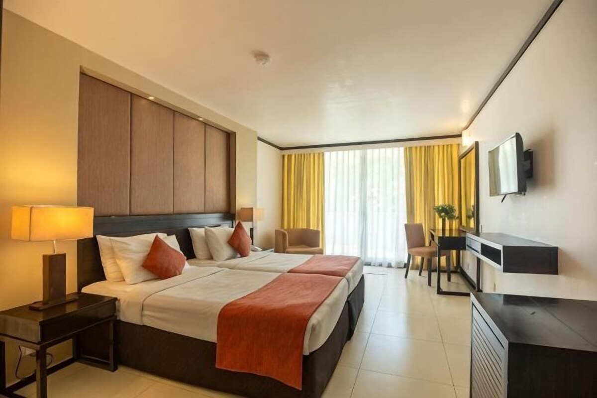 Une chambre d’hôtel avec un grand lit, deux tables de chevet, un bureau, une chaise, une télévision et une fenêtre avec des rideaux.