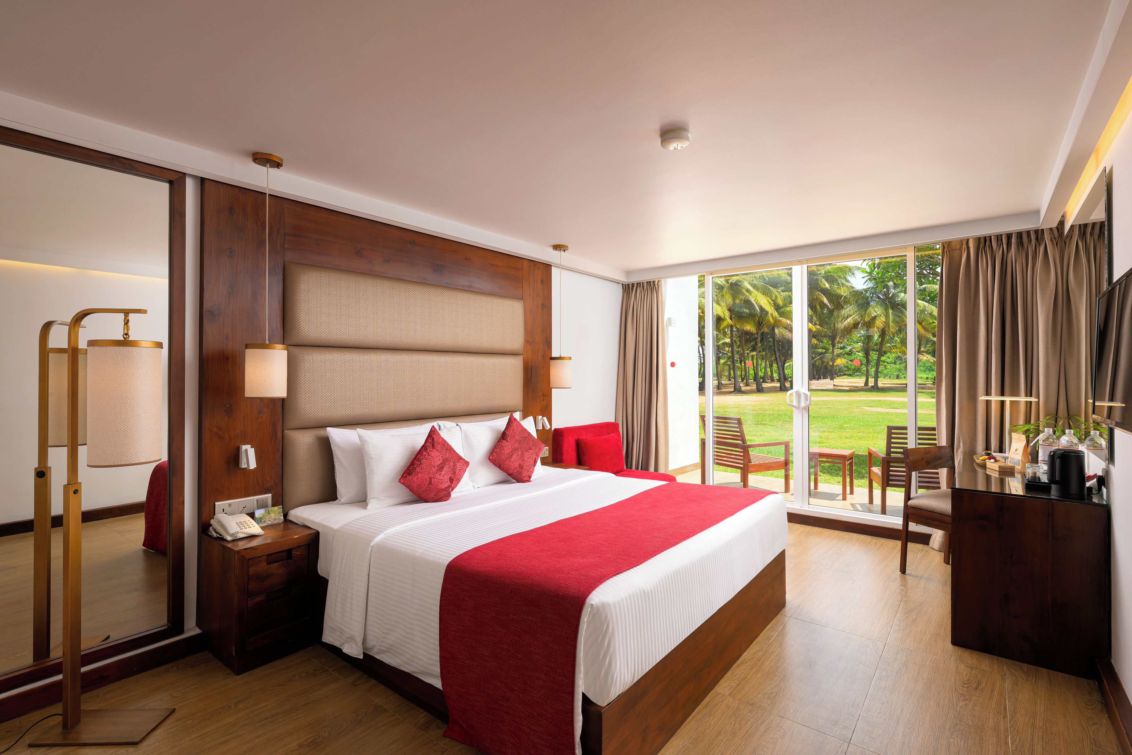 Habitación de hotel con una cama grande, una mesita de noche, un escritorio con cafetera y vistas a un jardín a través de la ventana.