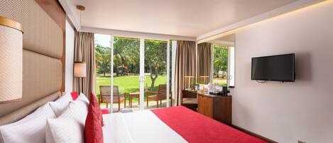 A hotel room with a bed, a desk, a TV, and a view of a garden.