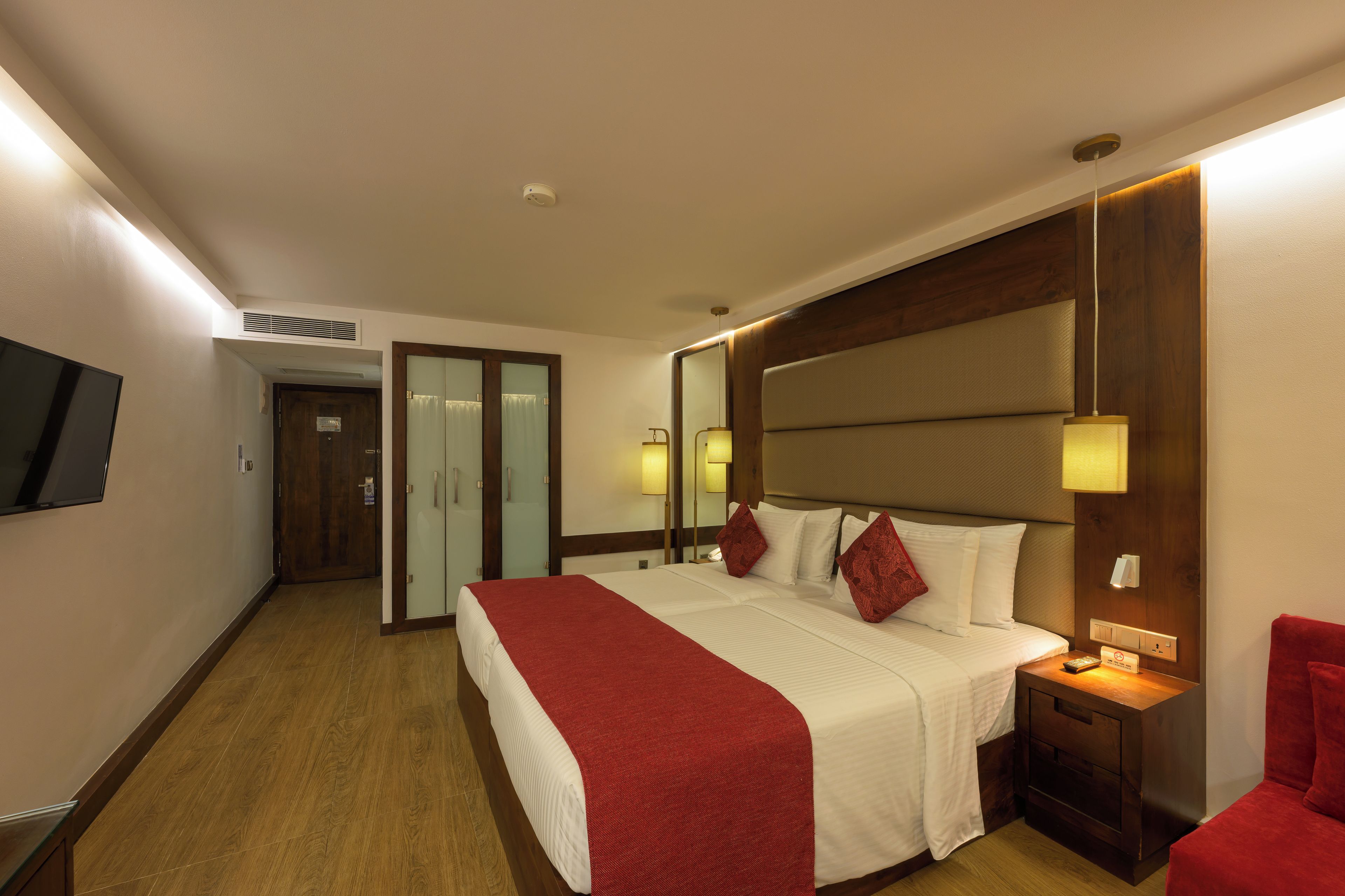A hotel room with a large bed, a television, a desk, and a red chair.