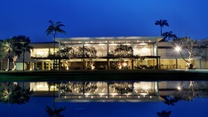 Un hotel moderno con una piscina reflectante al frente, amplias ventanas y palmeras.