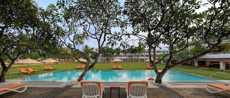 A poolside area with lounge chairs and umbrellas, surrounded by trees.