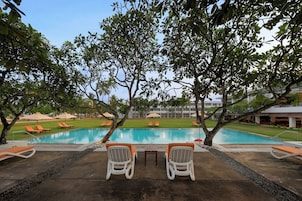 Zona de piscina con sillones de descanso y sombrillas, rodeada de árboles.