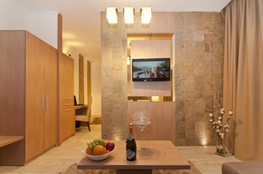 A modern room with a wooden cabinet, a television mounted on a stone wall, a table with a bottle of champagne and a bowl of fruit, and a vase with flowers.