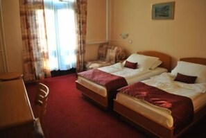 Une chambre d’hôtel avec deux lits simples, une chaise en bois, un bureau et une fenêtre avec des rideaux.