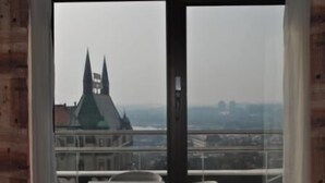 A view from a room with a large window overlooking a cityscape, including a prominent building with two spires. - Hotel Kasina (Belgrade)