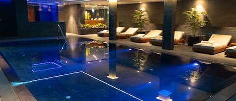 A modern indoor pool area with lounge chairs and potted plants.