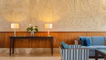 Un vestíbulo con pared de madera, un sillón a rayas, un sofá, una mesa con dos lámparas y un jarrón con flores.