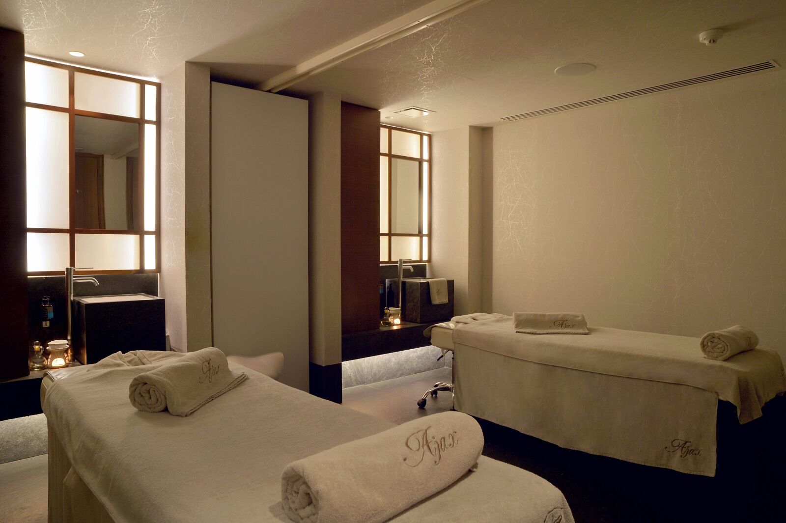 Habitación de hotel con dos camas, un espejo grande, un lavamanos y una camilla de masaje.
