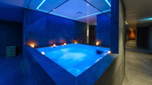 A modern spa room with a large, illuminated hot tub, geometric ceiling design, and ambient lighting. - Ajax Hotel (Limassol)