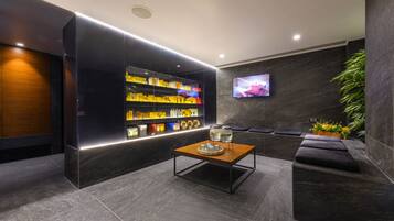 A modern lobby with a dark-toned reception desk, a glass display case with products, a flat-screen TV, and a seating area with a plant.